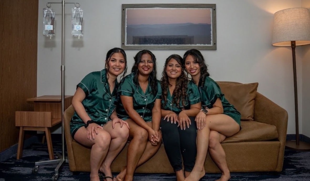 Four women in matching emerald satin pajamas on a hotel couch with a mobile IV pole and two A&M IV Co. drip bags set up beside them — bachelorette weekend in Nashville.